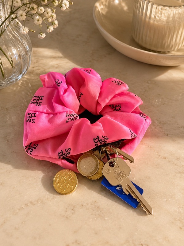Das rosa Scrunchie geöffnet, ein Schlüsselbund und mehrere Euromünzen liegen halb darin